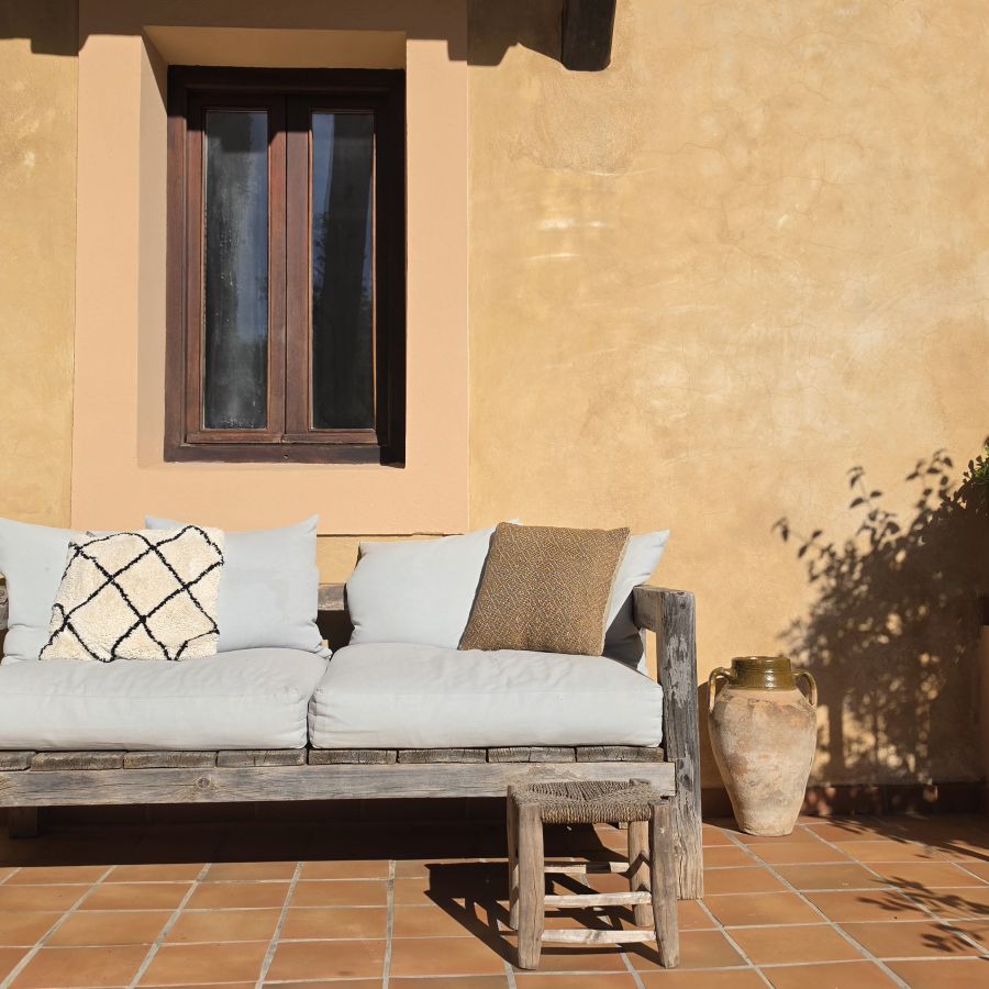 The sunny terrace at Casa Naya Ibiza, featuring a wooden sofa, terracotta pots and traditional Ibizan architecture